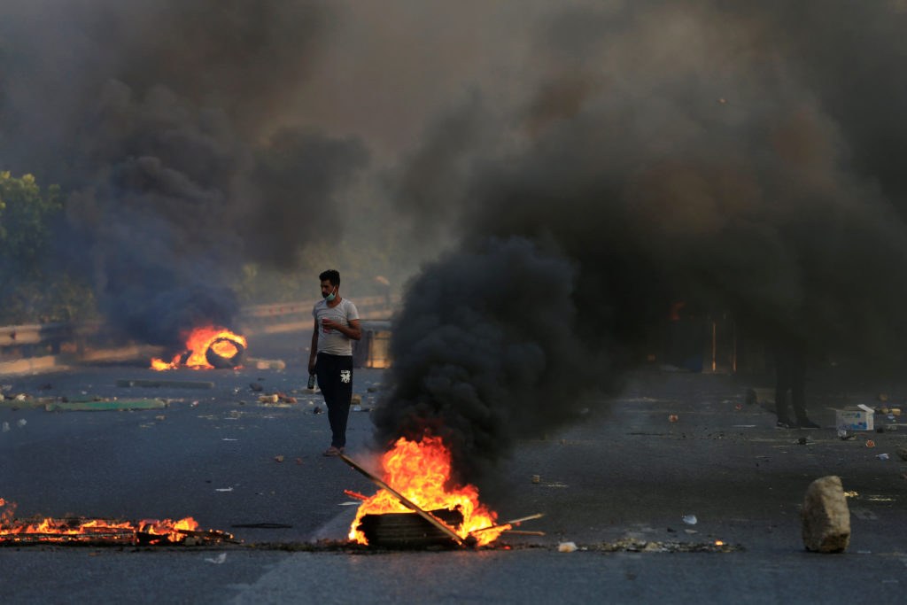 A man walks between burning tires and objects during a curfew, two days after the nationwide anti-government protests turn...