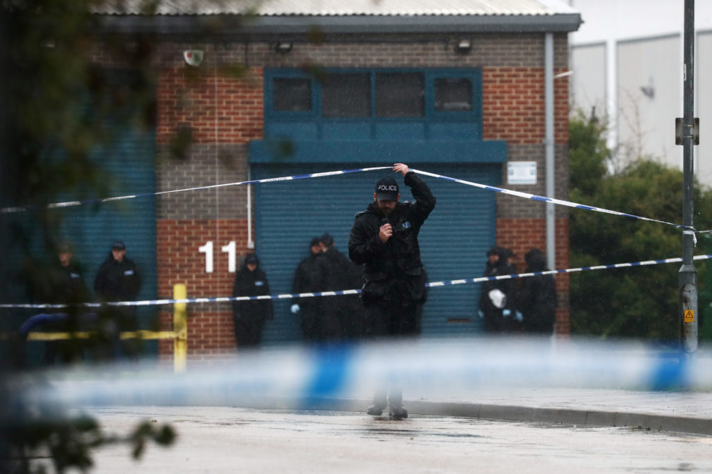 A police officer moves the tape inside the cordon, at the scene where bodies were discovered in a lorry container, in Gray...
