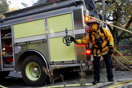 A firefighter passes a hose nozzle while working on a burning structure at the Kincade fire in Calistoga, California, U.S. October 29, 2019. Photo by Stephen Lam/Reuters