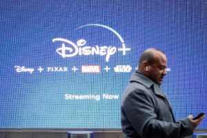 A man looks at his phone as he passes by a screen advertising Walt Disney's streaming service Disney+ in New York City, U.S., November 12, 2019. Photo by REUTERS/Brendan McDermid