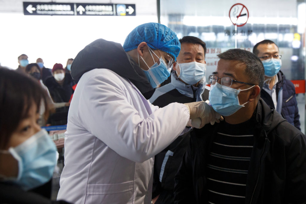 A medical official takes the body temperature of a man at the departure hall of the airport in Changsha, Hunan Province, a...