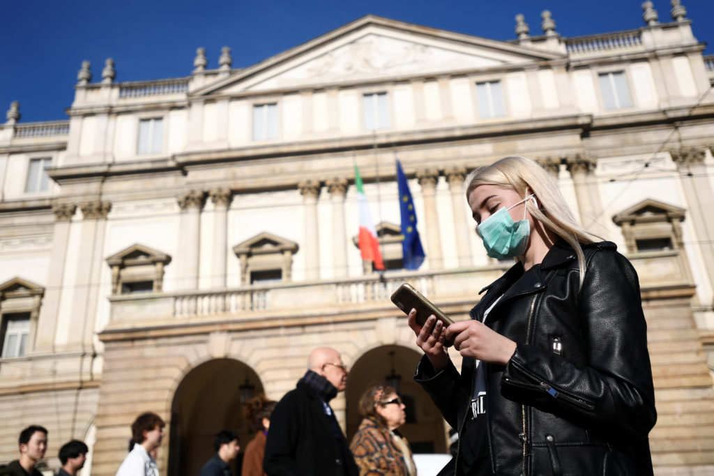 A woman wearing a face mask checks her phone outside the Teatro alla Scala, closed by authorities due to a coronavirus out...