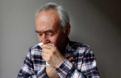 Older man coughing into napkin