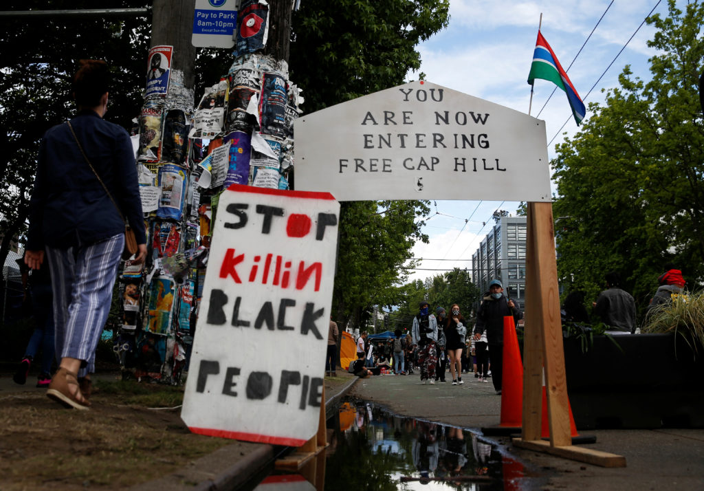 FILE PHOTO: People walk by signs at a barrier set up at the edge of the self-proclaimed CHAZ/CHOP zone around the Seattle ...