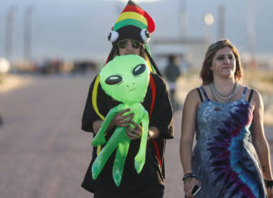 Two people walk outside Area 51 holding a balloon alien.