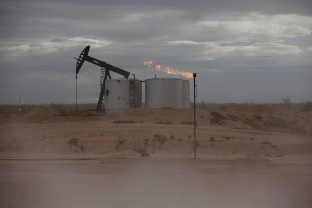 FILE PHOTO: Dust blows around a crude oil pump jack and flare burning excess gas at a drill pad in the Permian Basin in Lo...