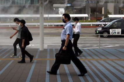 Commuters wearing protective masks make their through a cooling water mist in Tokyo