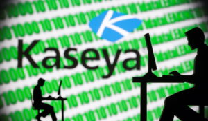3D printed models of men working on computers are seen in front of a displayed Kaseya logo