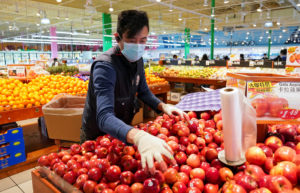 Wearing a mask and gloves, a worker re-stocks apples in a Asian grocery store in Falls Church, Virginia