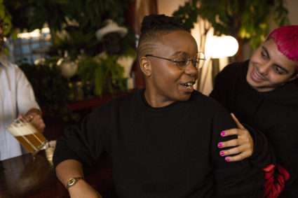 A transmasculine person with a friend at a bar.