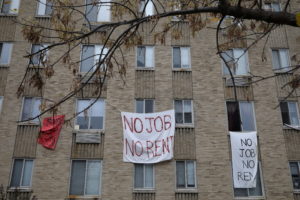 Makeshift sheets displaying messages of protest contesting the ability to pay for rent hang in a window of an apartment bu...