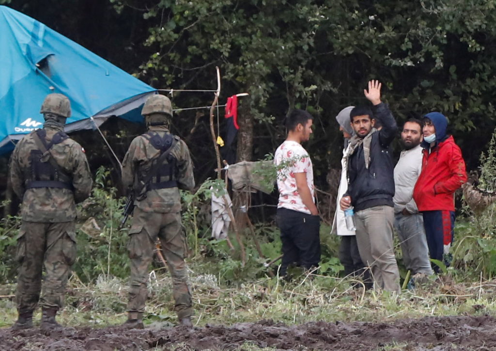 Polish border guard officers stand guard next to a group of migrants stranded on the border between Belarus and Poland nea...