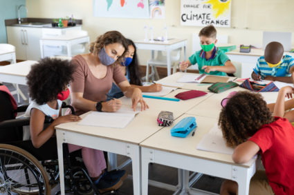 Female teacher wearing face mask teaching a disable girl in class