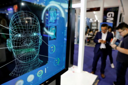 FILE PHOTO: Visitors check their phones behind the screen advertising facial recognition software during Global Mobile Int...
