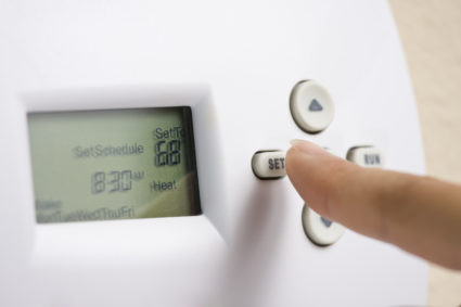A person sets an electronic thermostat heat to 68 degrees.
