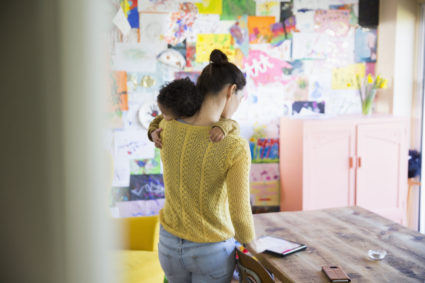 Mother holding baby son, using digital tablet at dining table