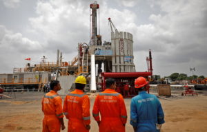 Technicians stand next to an oil rig which is manufactured by Megha Engineering and Infrastructures Limited (MEIL) at an O...