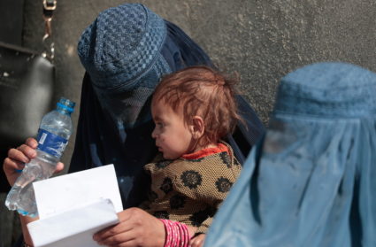 Displaced Afghan woman holds her child as she waits with other women to receive aid supply outside an UNCHR distribution c...