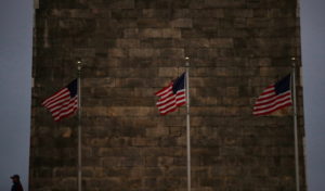 A woman stands in front of the Washington Monument as U.S flags flutter in the wind in Washington