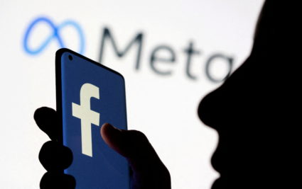 FILE PHOTO: Woman holds smartphone with Facebook logo in front of a displayed Facebook's new rebrand logo Meta in this ill...