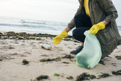 Female environmentalist collecting bottle in garbage bag while crouching at beach