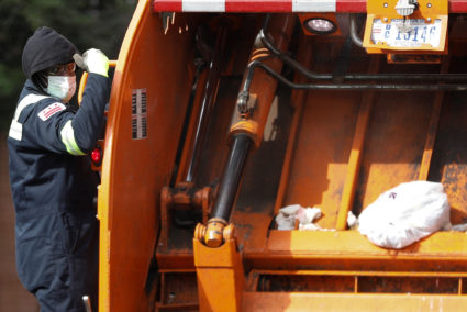 A waste management employee rides on a garbage truck wearing a face mask and gloves, as Mayor Muriel Bowser issued a State...