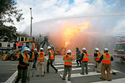 PG&amp;E officials are seen as firefighters battle a fire following an explosion at Geary boulevard and Parker Avenue in S...