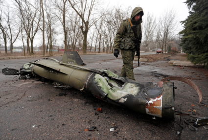 A militant of the self-proclaimed Donetsk People's Republic inspects the remains of a missile that landed on a street in D...