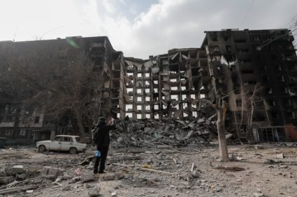 A local resident walks near a damaged block of flats in the besieged city of Mariupol