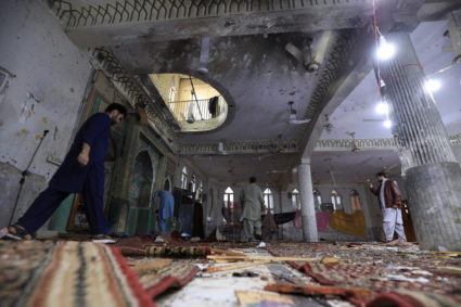 People walk amid the damages at the prayer hall after a bomb blast inside a mosque during Friday prayers in Peshawar