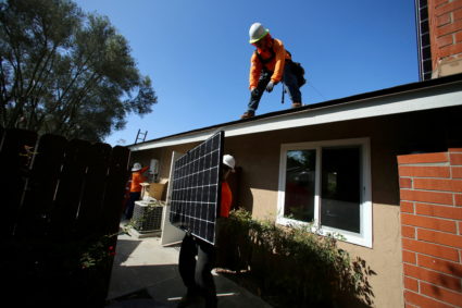 FILE PHOTO: Workers lift a solar panel onto a roof during a residential solar installation in Scripps Ranch, San Diego, Ca...