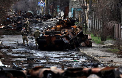 A soldier takes a photograph of his comrade as he poses beside a destroyed Russian tank and armoured vehicles, amid Russia...