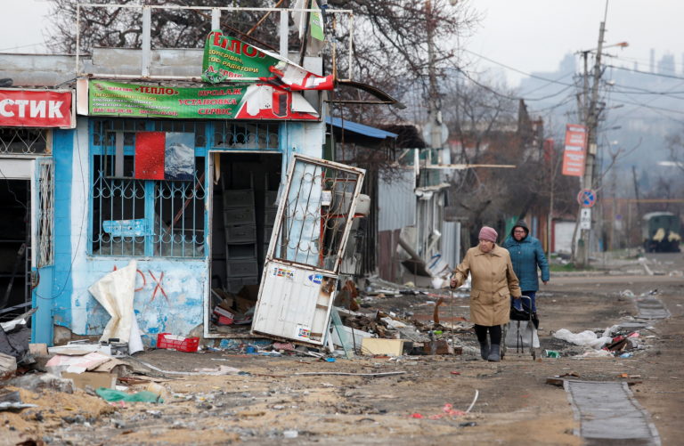 Women walk past damaged kiosks in Mariupol