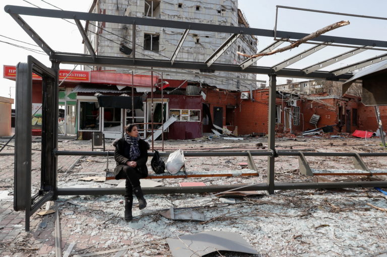 A woman sits on a bench at a damaged bus stop in Mariupol