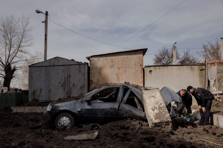 Men look into their car to retrieve belongings after it was damaged when a rocket exploded next to it in Kharkiv