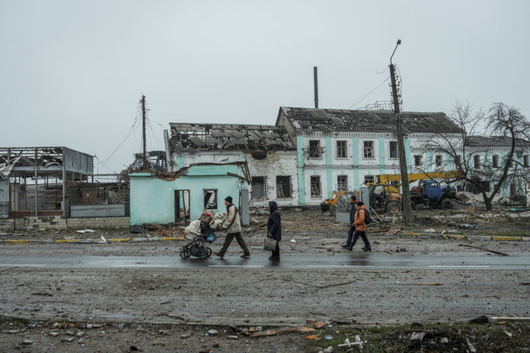 Local residents walk past buildings damaged by shelling in the town of Makariv