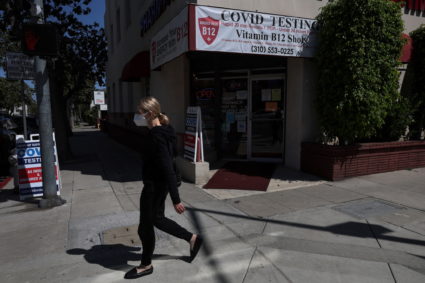 A woman wearing a protective face mask walks by a Covid-19 testing site on a street corner in Beverly Hills