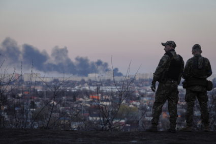 Ukrainian soldiers look at a column of smoke that rises from the Kulinichi bread factory after it was hit by shelling in K...