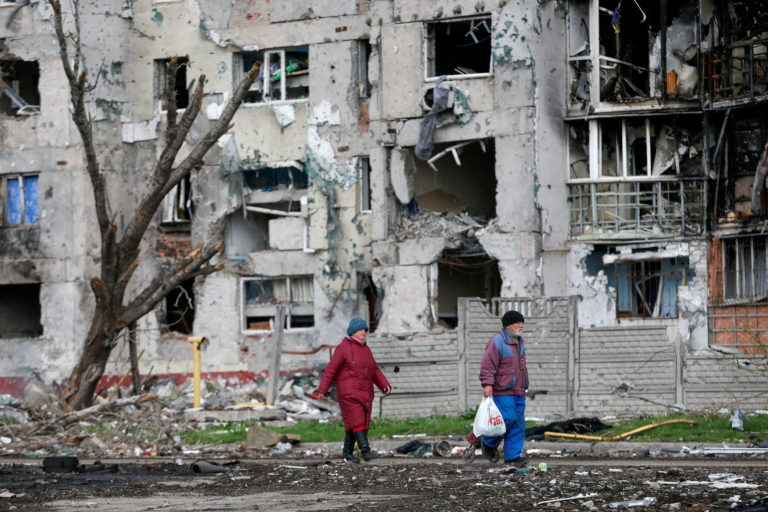 FILE PHOTO: FILE PHOTO: People walk near a destroyed residential building in Mariupol