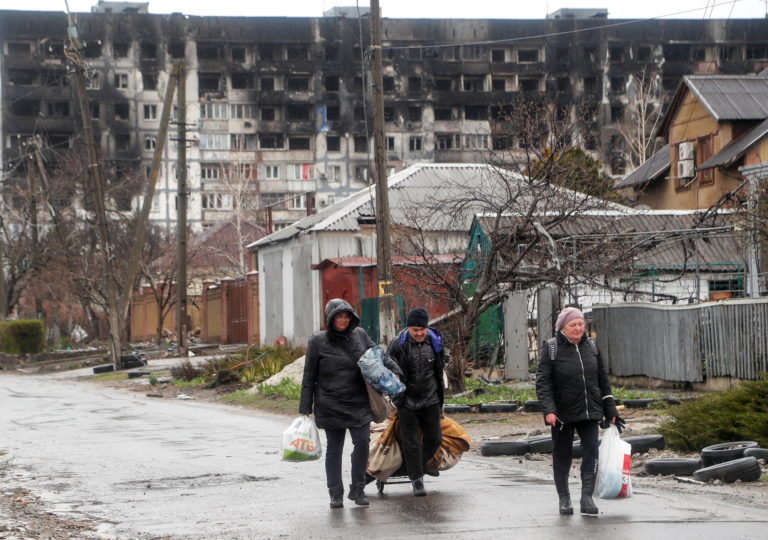 Local residents walk in front of a damaged residential building in Mariupol