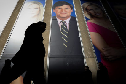 People pass by a promo of Fox News host Tucker Carlson on the News Corporation building in New York