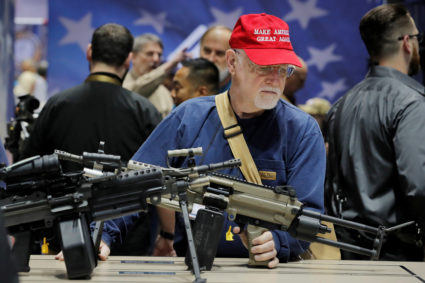 A man wearing a Make America Great Again hat inspects a Fabrique Nationale America LLC rifle during the National Rifle Ass...