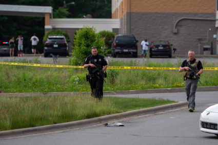 Police carry long guns searching for evidence after an