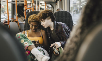 Teenage boy looking at young non-binary woman using smart phone in bus
