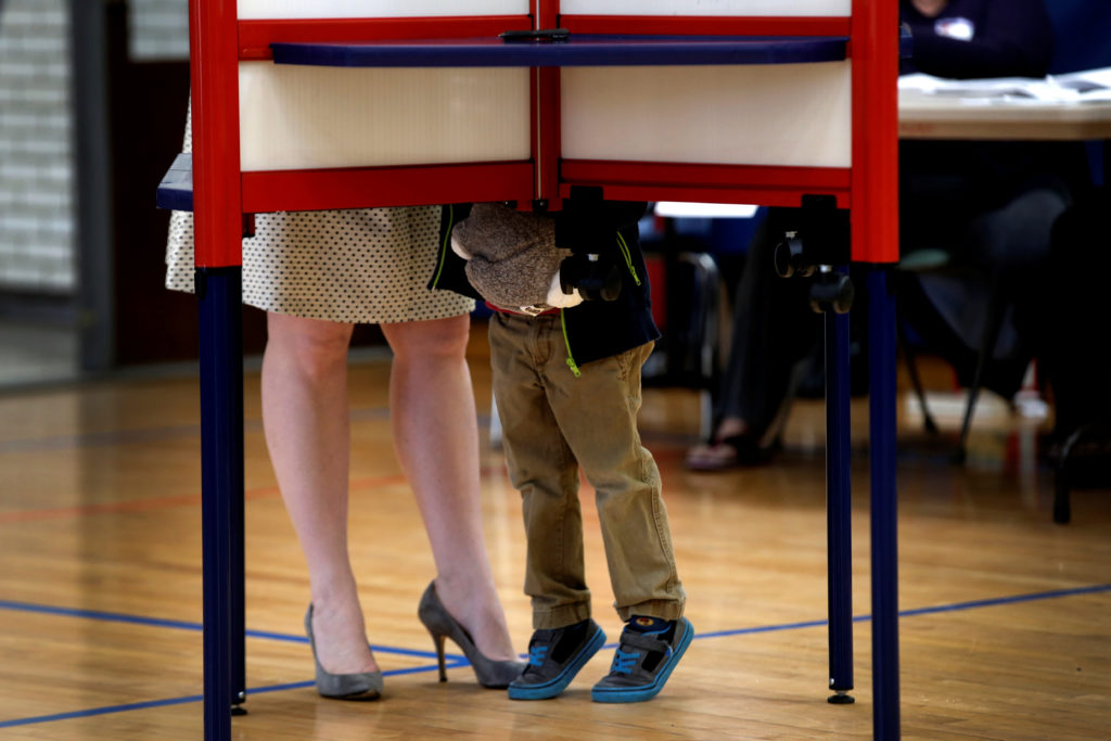 A woman fills out her ballot in a voting booth in the New York U.S. presidential primary election as her young son looks, ...