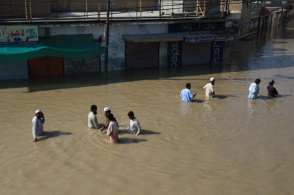 Residents wade along a flooded street, following rains and floods during the monsoon season in Nowshera