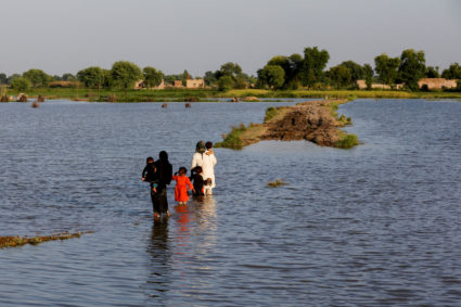 A family walks amid flood waters on their way to their village, following rains and floods during the monsoon season in Mehar