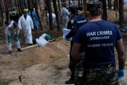 A war crimes prosecutor stands as experts work at a forest grave site during an exhumation in Izium