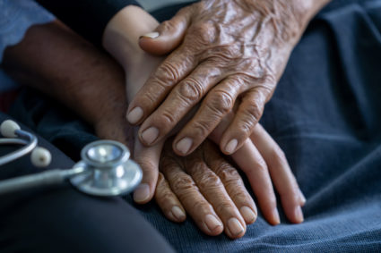 Close up of young nurse holding old man's hands and encourage him.