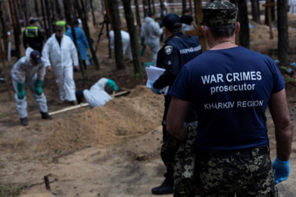 A war crimes prosecutor stands as experts work at a forest grave site during an exhumation in Izium